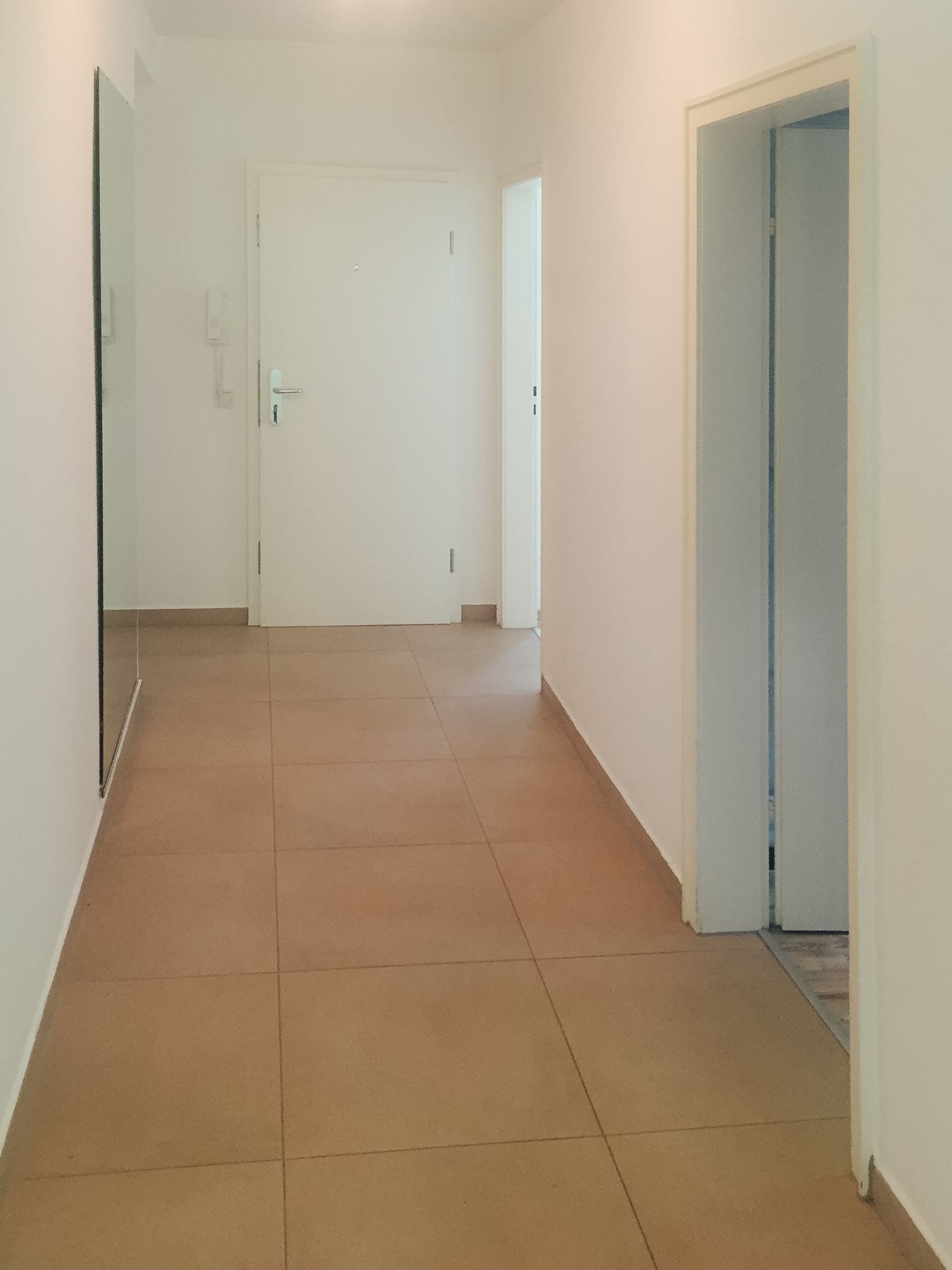 Heller Flur mit beige gefliesten Boden, mehreren Türen und weiß gestrichenen Wänden.