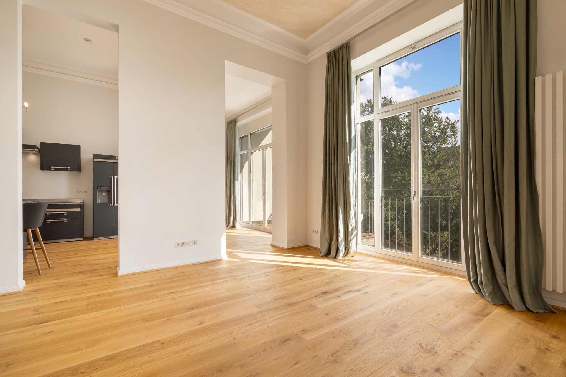 Helles Wohnzimmer mit Parkettboden, großen Fenstern und Blick in eine moderne Küche.