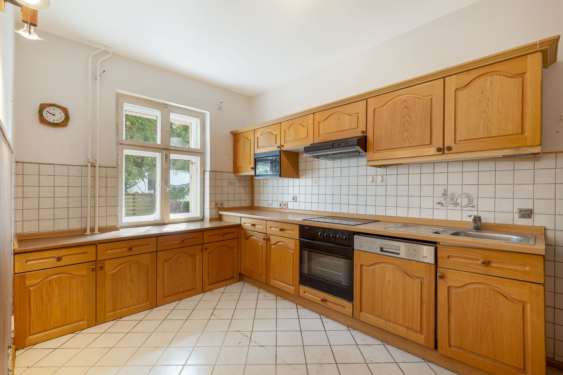 Helle Küche mit Holzmöbeln, Elektroherd, Spülmaschine und großem Fenster.