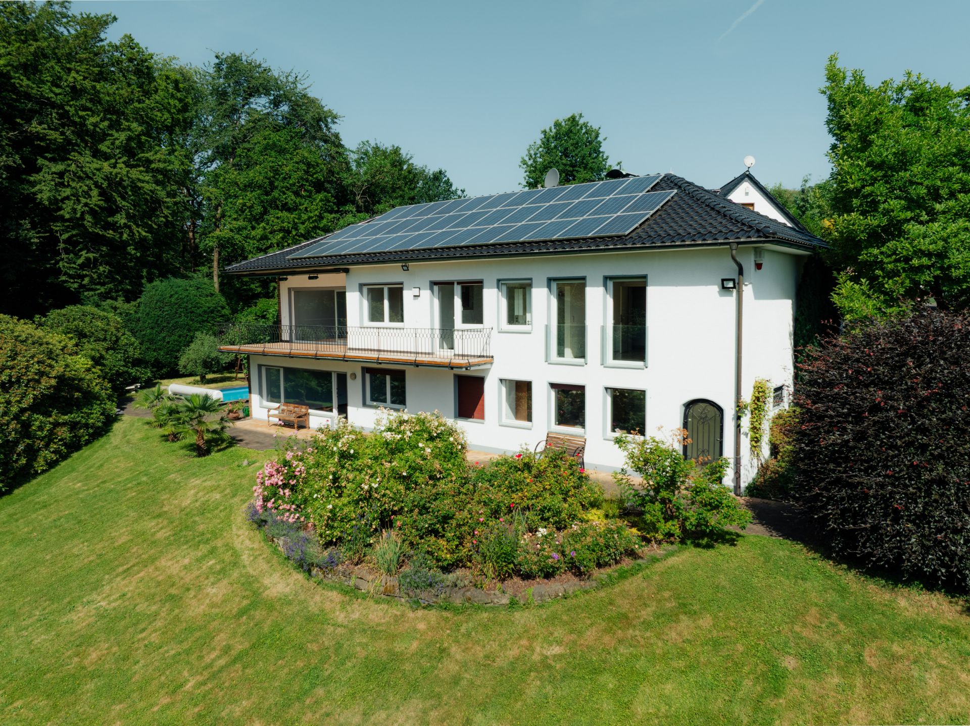 Weißes Wohnhaus mit Solarpanelen auf dem Dach und Garten mit Blumen und Bäumen.