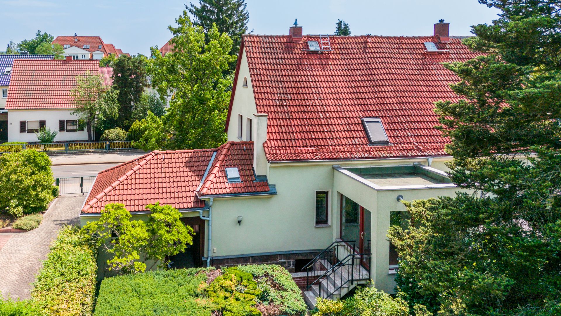 Wohnhaus mit rotem Satteldach, Zugangstreppe und umgeben von Bäumen und Büschen.