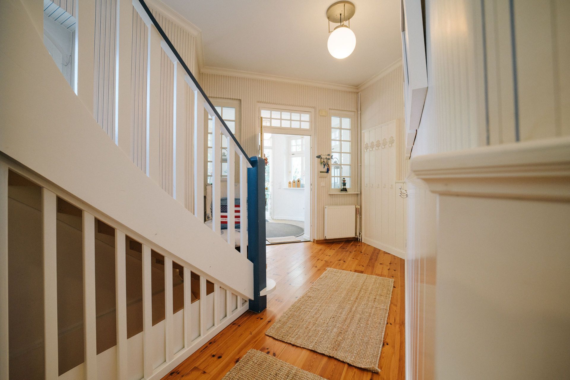 Heller Flur mit Holztreppe, Holzboden, Teppichen und Lampe an der Decke.