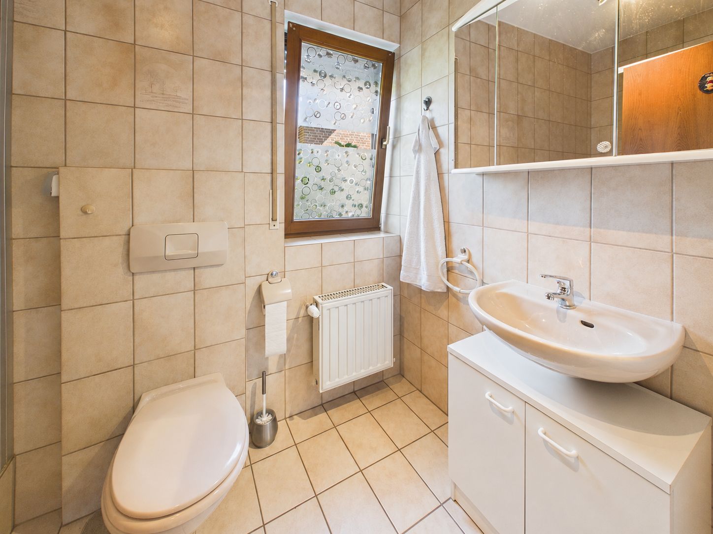 Helles Badezimmer mit WC, Waschbecken, Spiegel und Fenster.