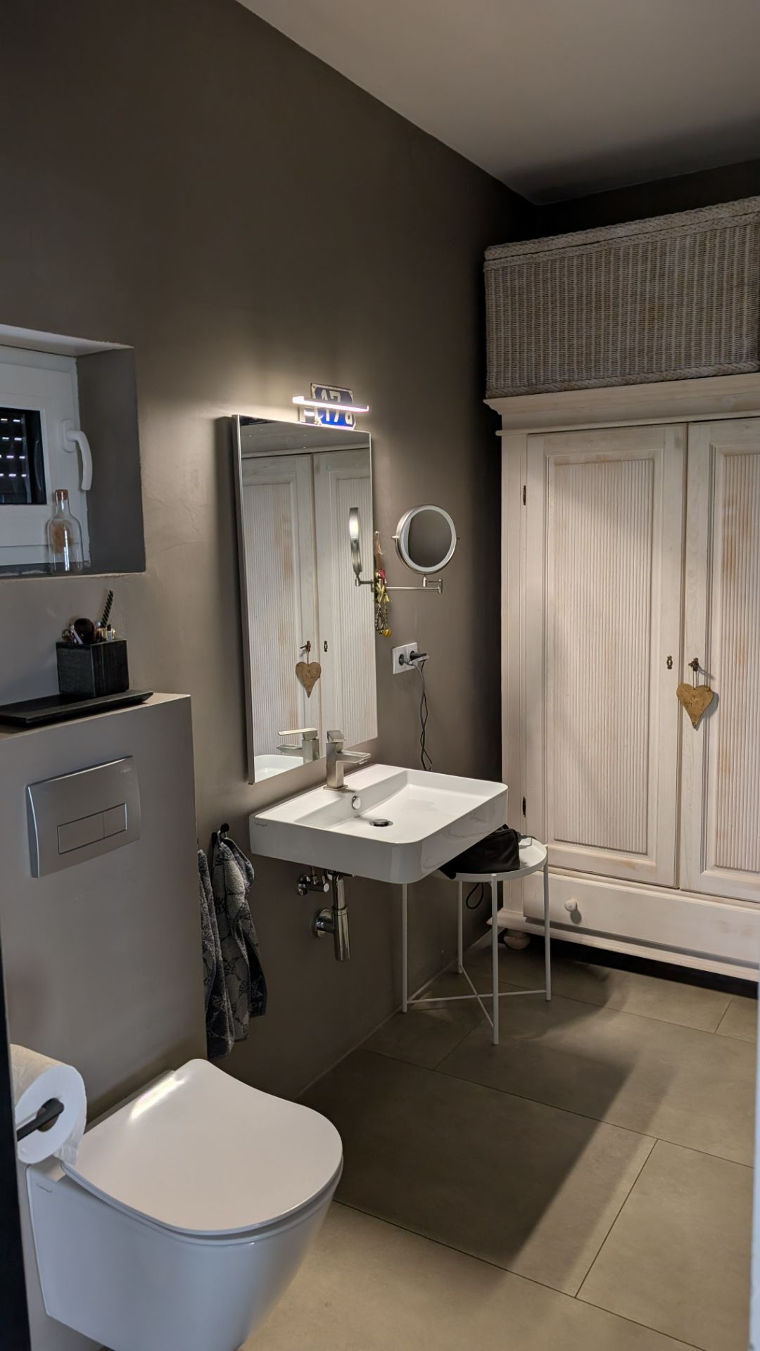 Modernes Badezimmer mit Waschbecken, Wandspiegel, Toilette und weißem Schrank.