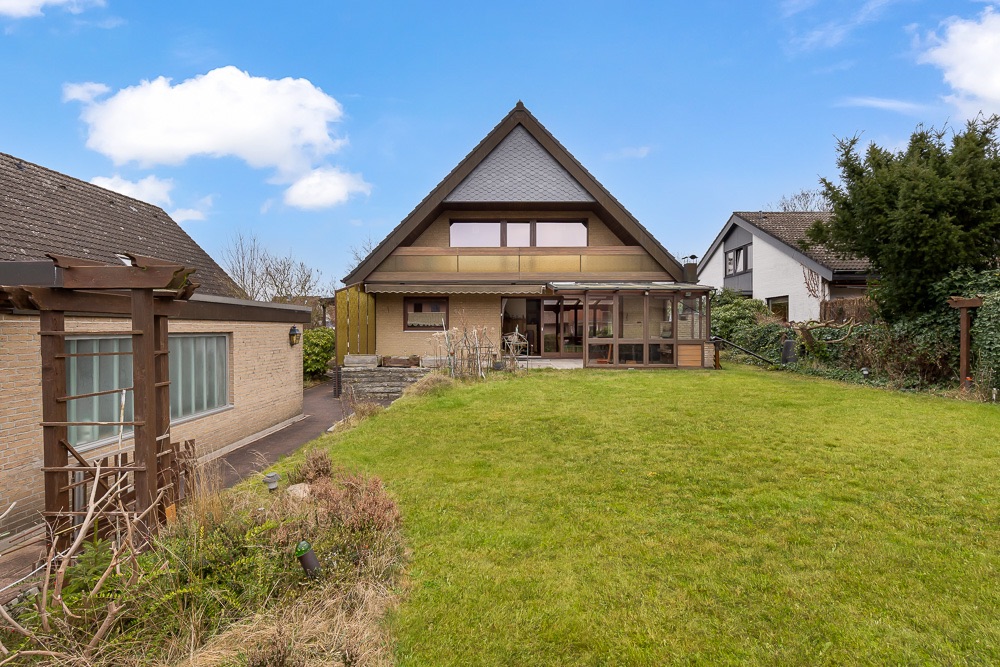 Haus mit großem Garten, Wintergarten und Dachgeschossfenstern, daneben weitere Wohnhäuser.