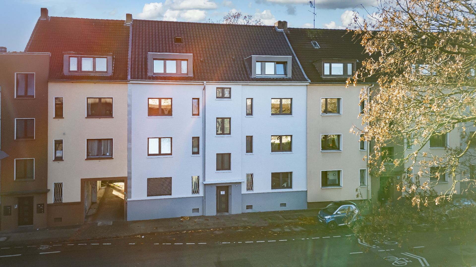 Mehrstöckiges Wohnhaus mit mehreren Fenstern und Eingängen an einer Straße.