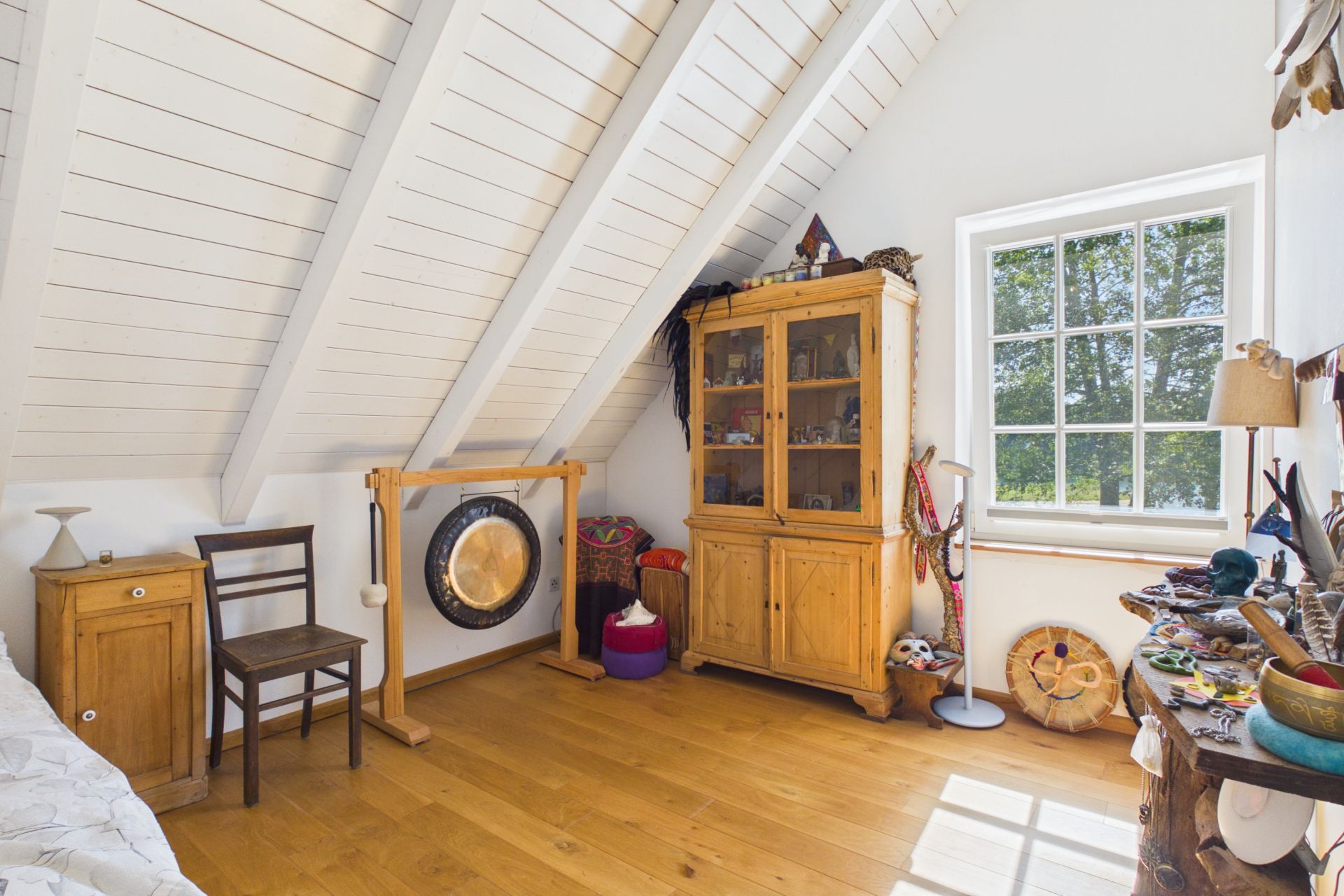 Heller Dachraum mit Holzschrank, Gong, Fenster und verschiedenen Dekorationen.