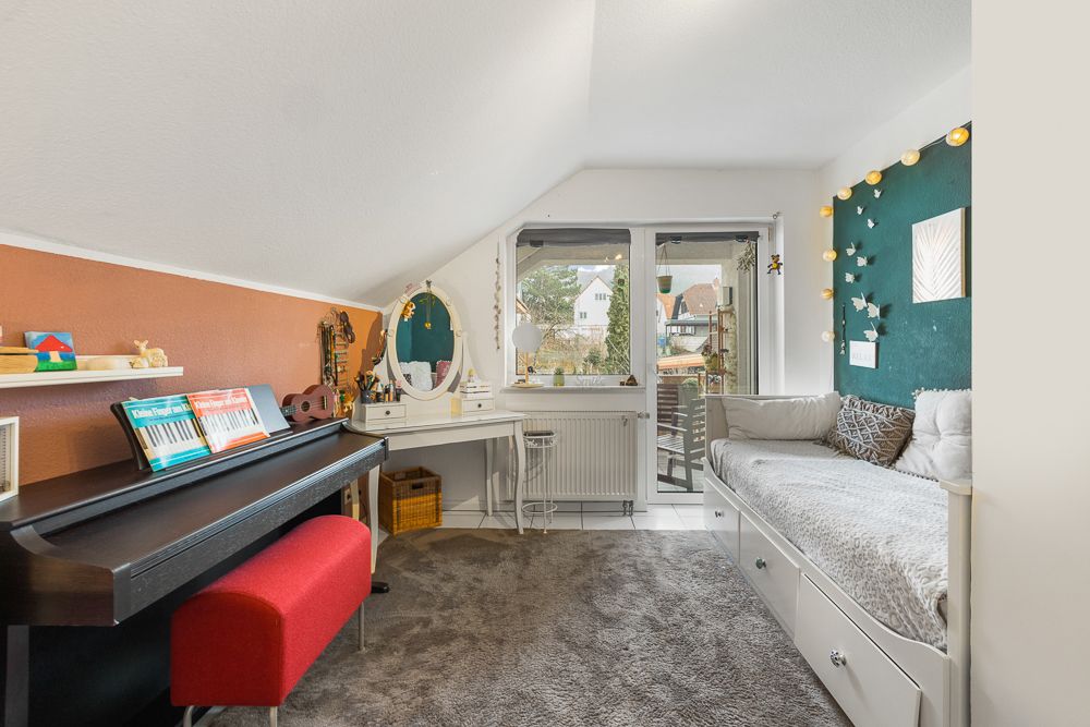 Helles Zimmer mit Klavier, Schminktisch, Bett und großem Fenster mit Blick nach draußen.