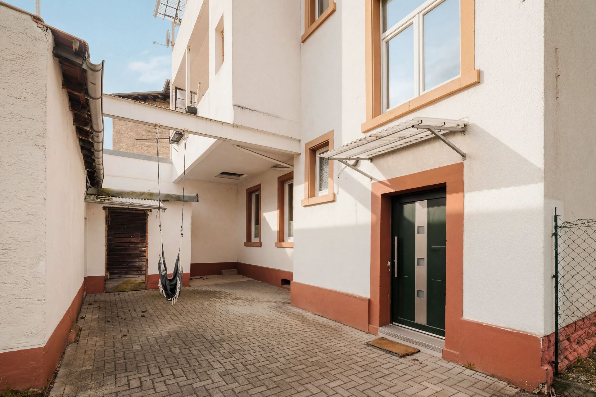 Gepflasterter Innenhof mit weißem Gebäude, Fenstern und einer Schaukel im Durchgang.