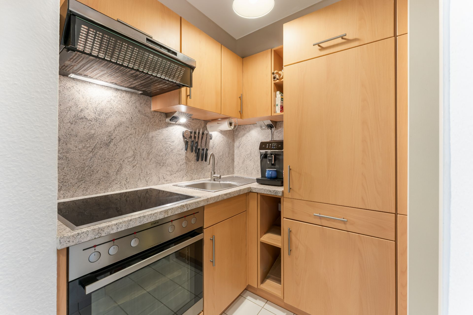 Moderne Einbauküche mit Holzfronten, Herd, Spüle, Kaffeemaschine und Hängeschränken.