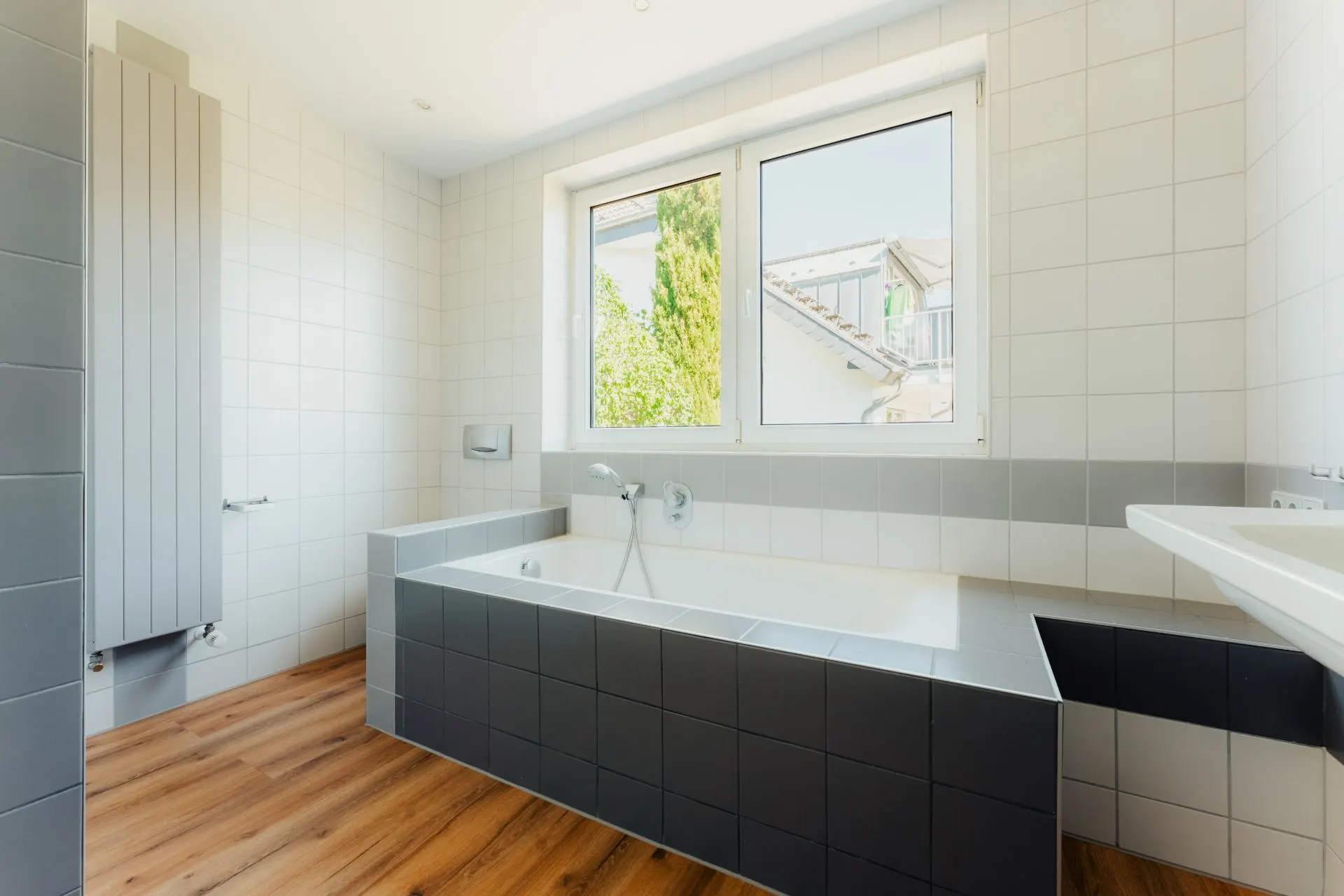 Helles Badezimmer mit Badewanne, großem Fenster und Fliesenboden in Holzoptik.