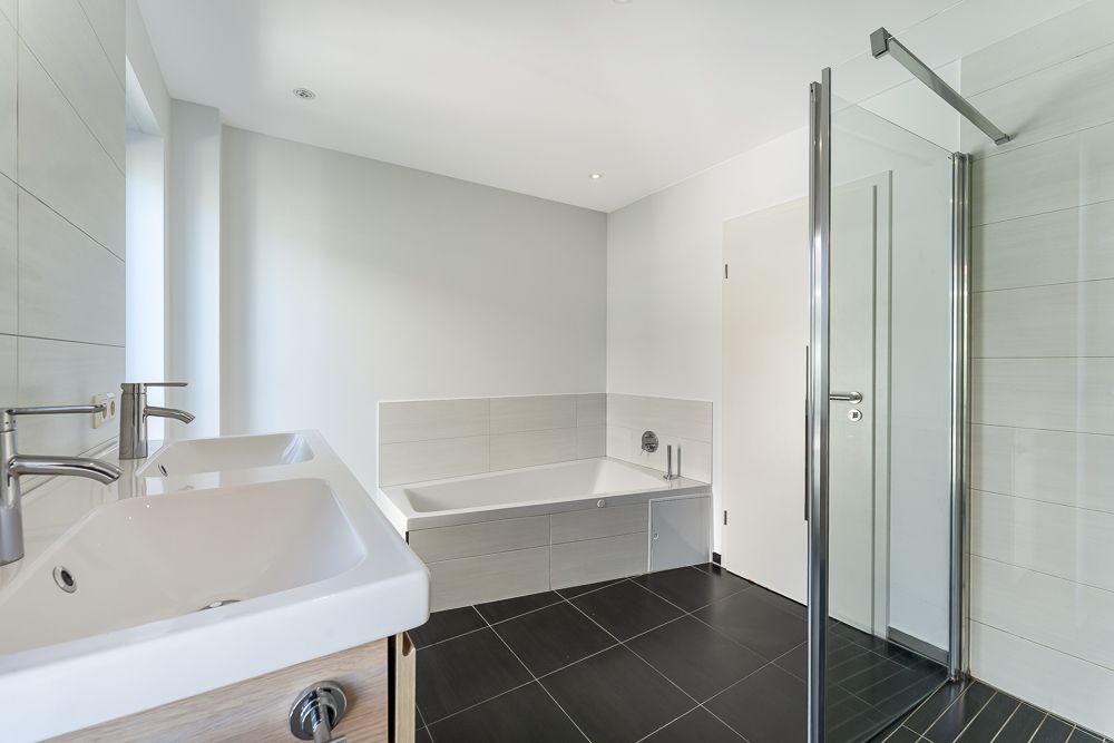 Modernes Badezimmer mit Badewanne, Dusche, zwei Waschbecken und schwarzen Fliesen.