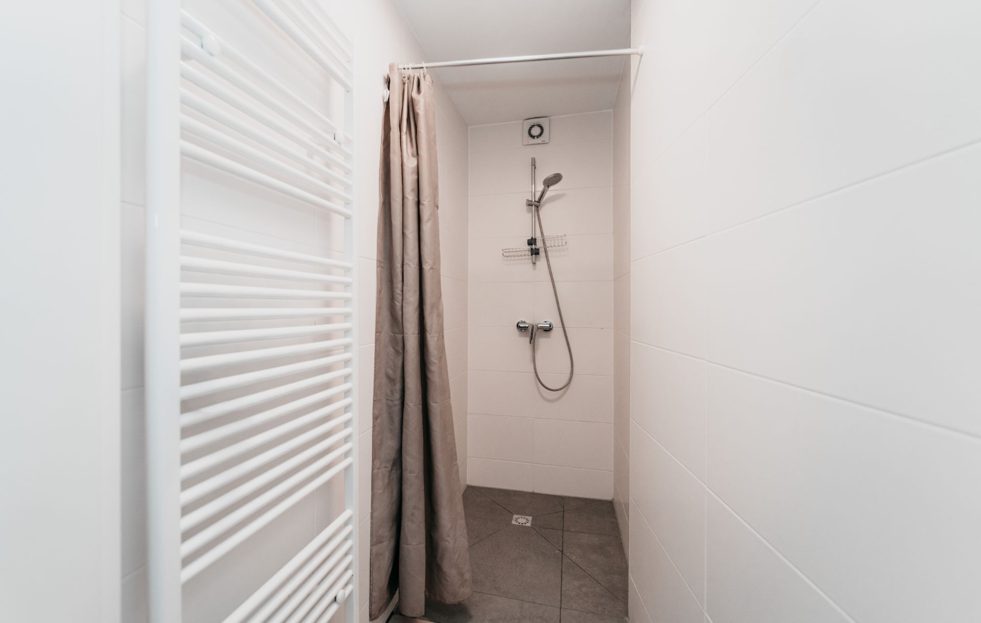 Dusche mit Duschvorhang, Handbrause und weißem Handtuchheizkörper an der Wand.