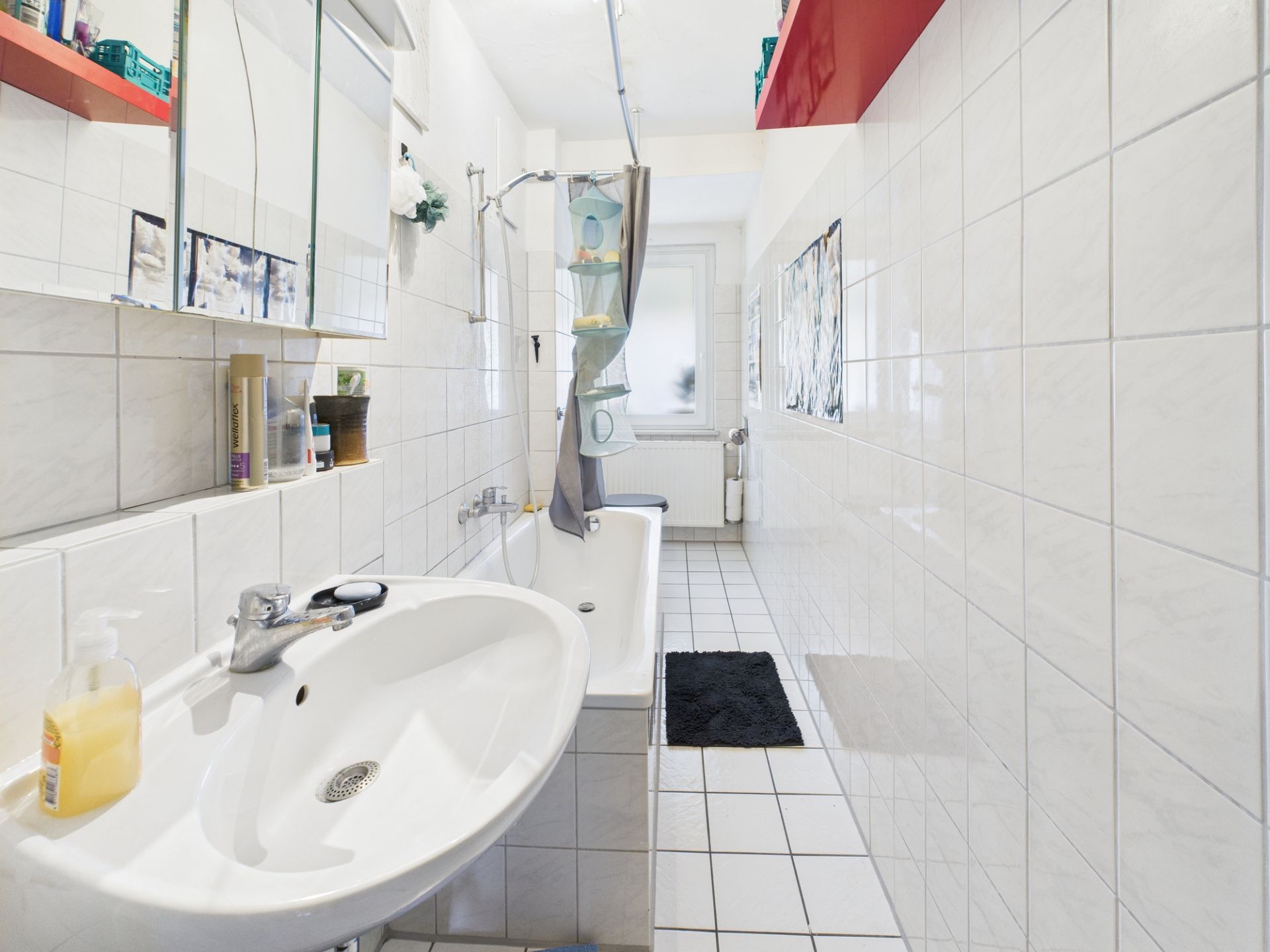 Helles Badezimmer mit Waschbecken, Badewanne, Duschvorhang und weißen Fliesen.