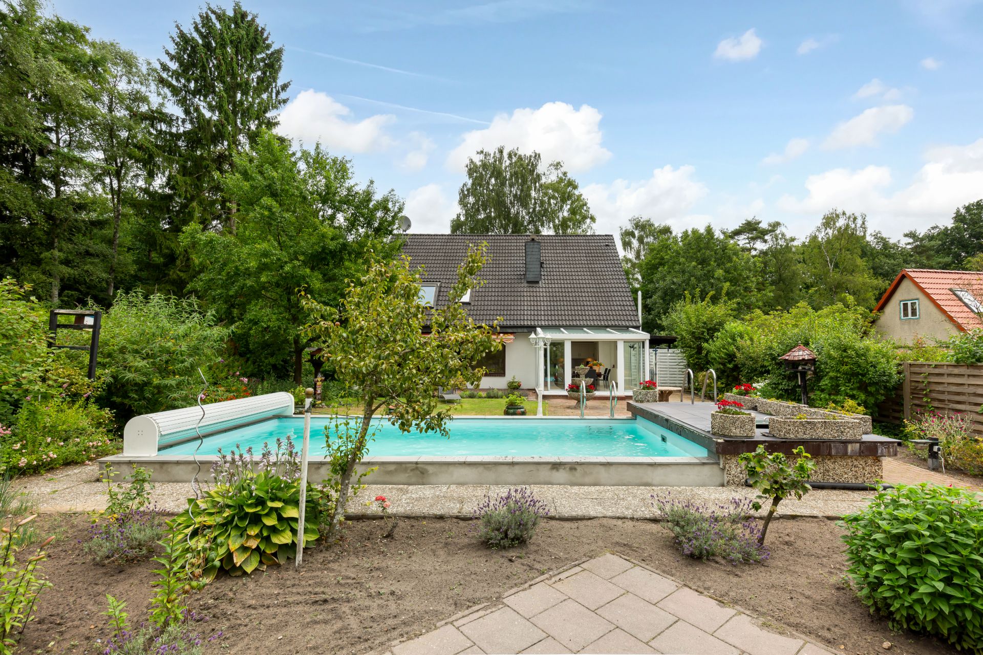 Garten mit Swimmingpool und Bäumen vor einem Einfamilienhaus.