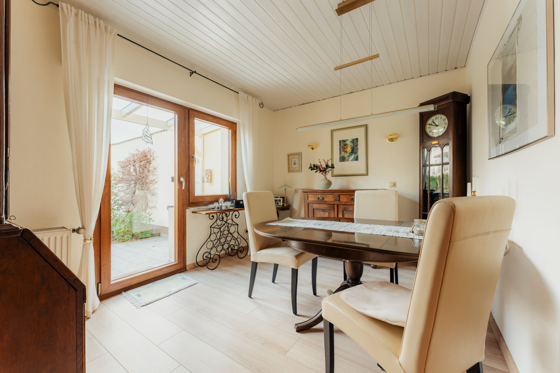 Esszimmer mit Glastisch, vier Stühlen, großer Uhr und Zugang zur Terrasse.