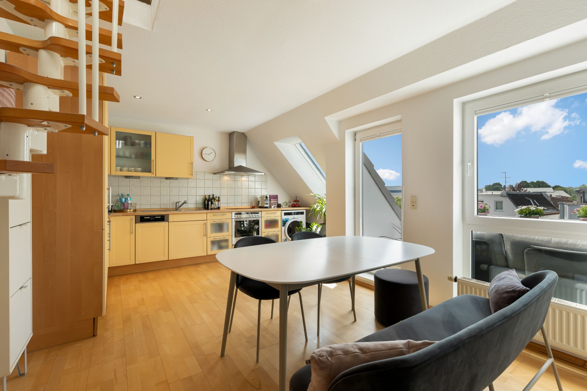 Helle Wohnküche mit Esstisch, Stühlen und Zugang zu einem Balkon, große Fenster im Raum.