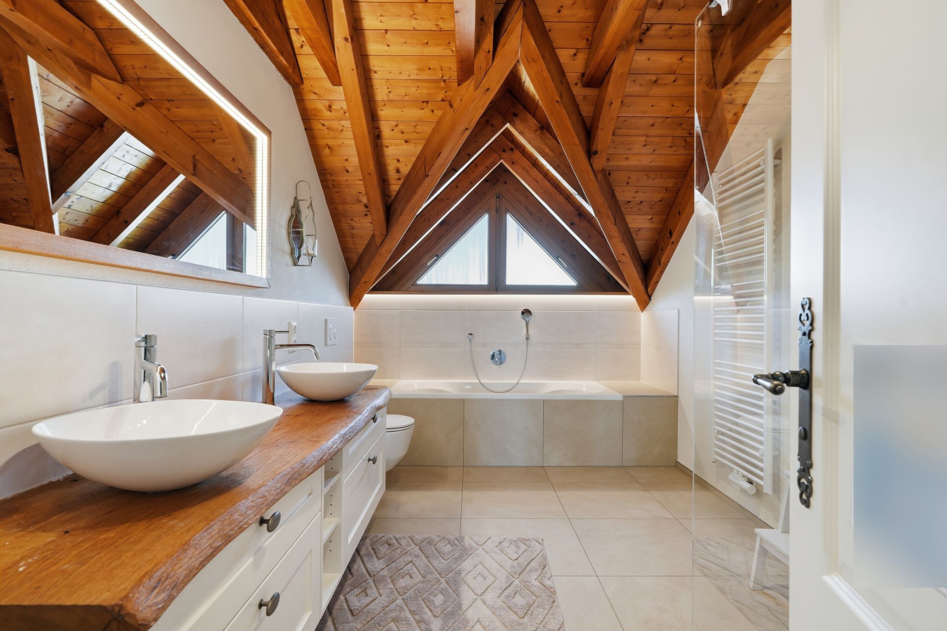 Modernes Badezimmer mit Holzdecke, zwei Waschbecken und Badewanne unter Dachfenster.