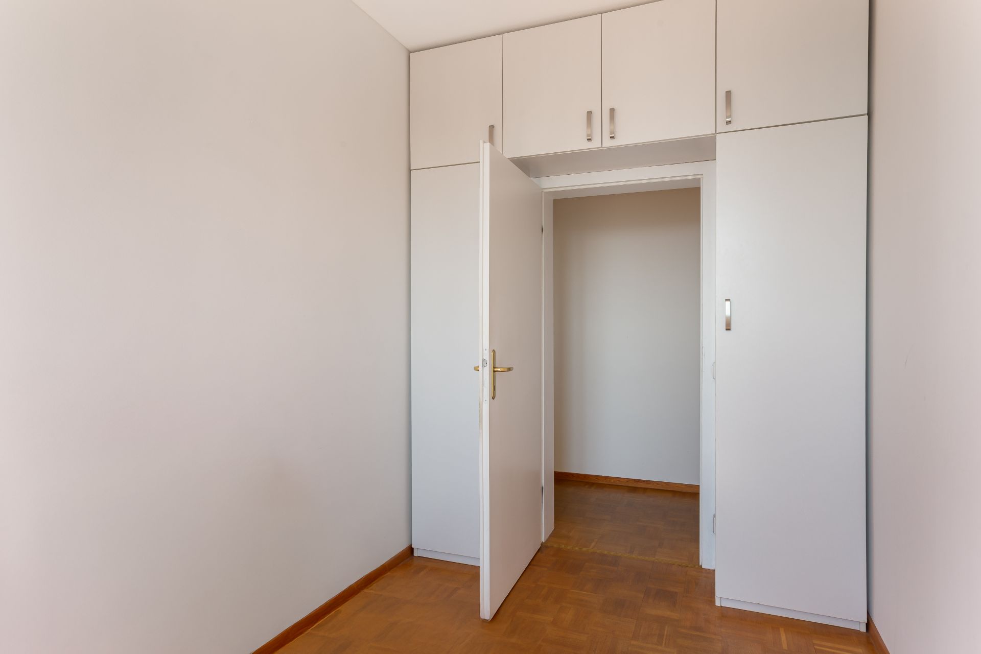 Leerer Raum mit Holzboden, weißer Tür und Einbauschränken an der Wand.