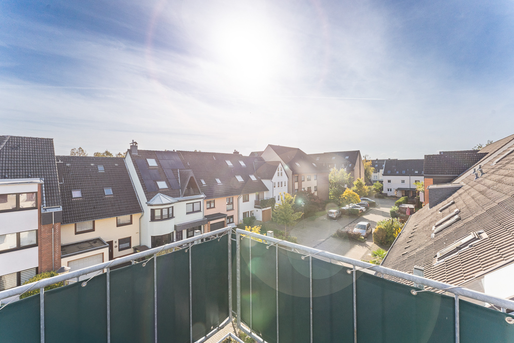 Blick von einem Balkon auf eine Wohnsiedlung mit Reihenhäusern an einem sonnigen Tag.