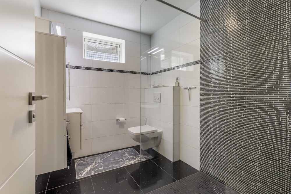 Modernes Badezimmer mit Wandtoilette, Waschtisch und großer, bodengleicher Dusche.
