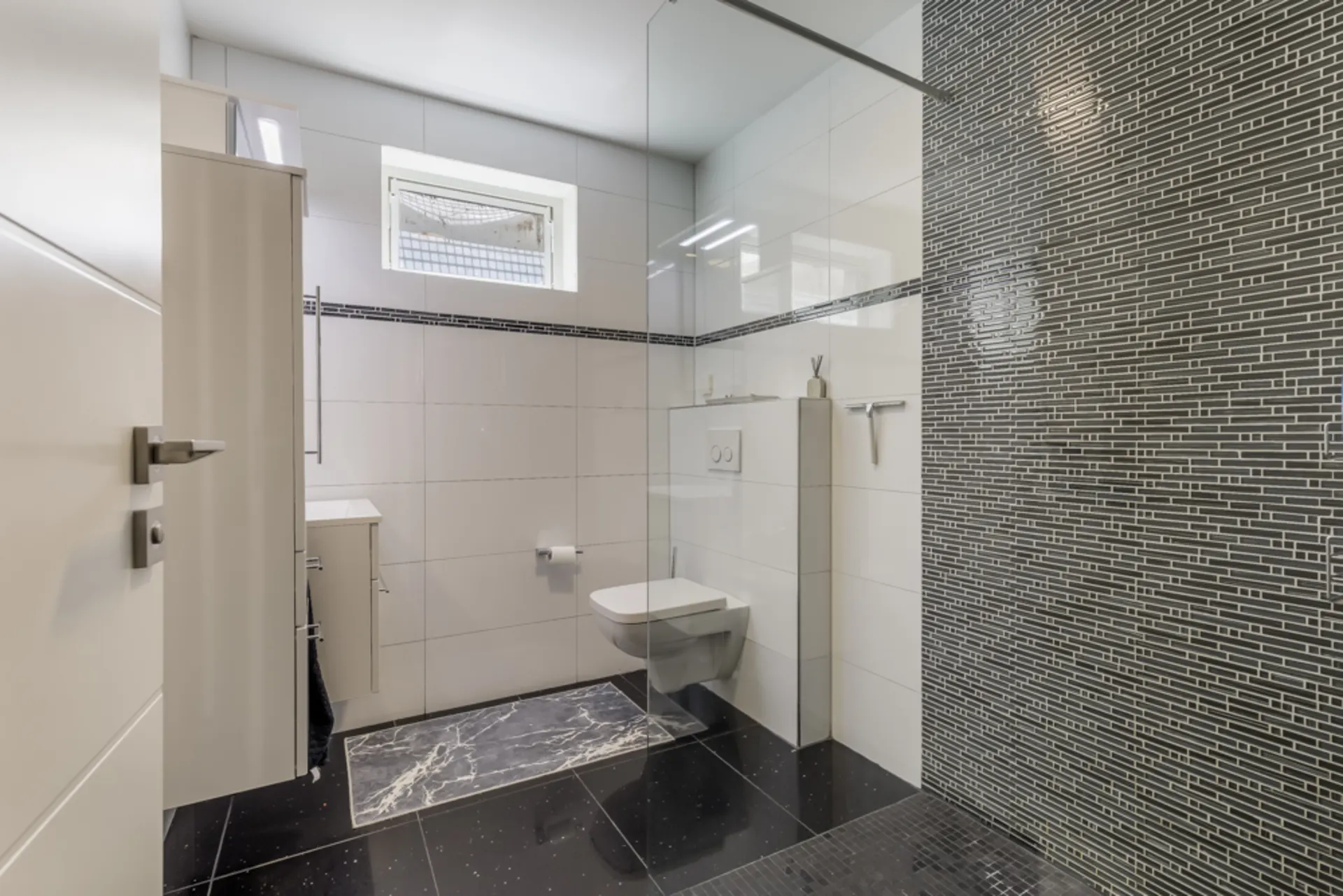 Modernes Badezimmer mit Wandtoilette, Waschtisch und großer, bodengleicher Dusche.
