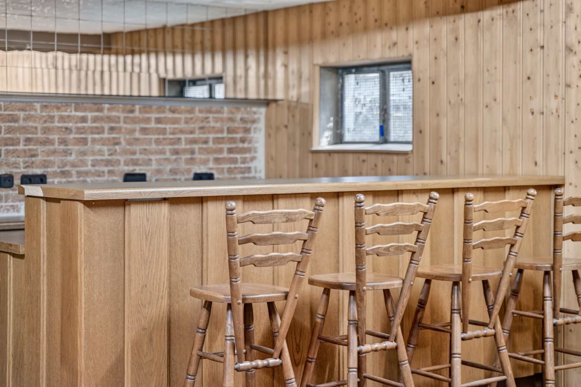 Holztheke mit vier Holzstühlen in einem Raum mit Holzvertäfelung und kleinem Fenster.