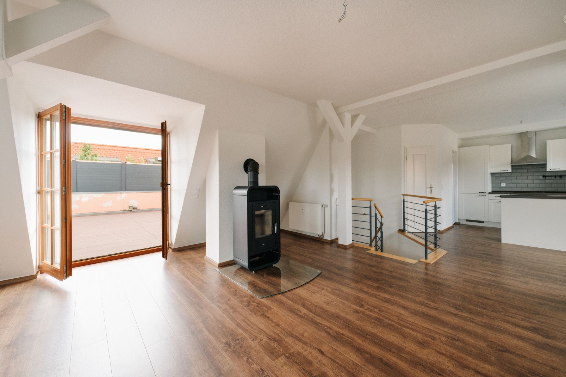 Heller Wohnraum mit Holzofen, offener Küche, Holzfußboden und Zugang zu einer Terrasse.