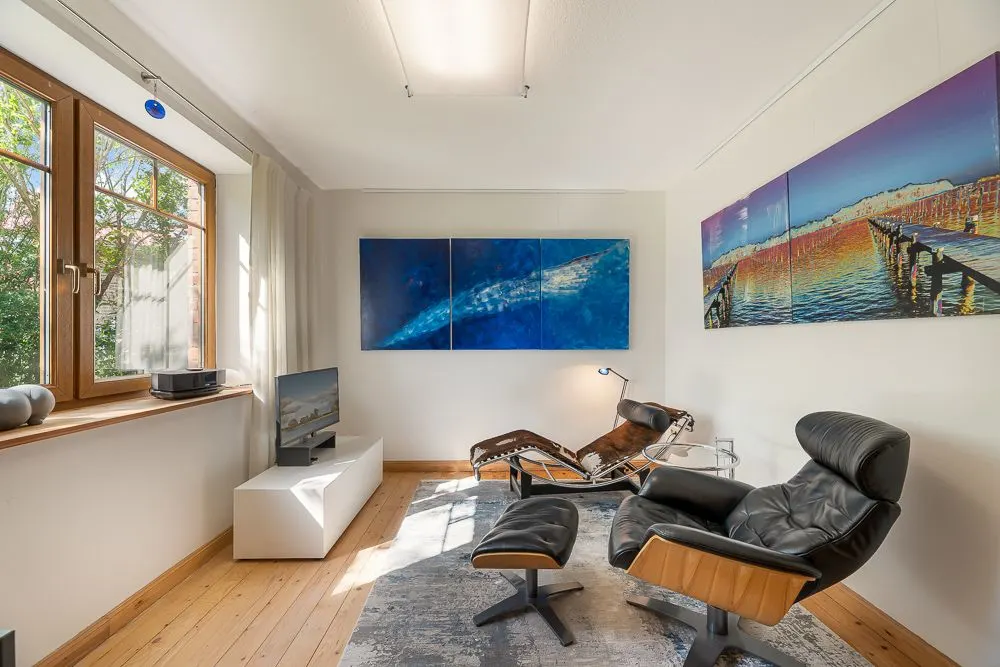 Helles Wohnzimmer mit zwei modernen Sesseln, Teppich, Fernseher und großen Wandbildern.
