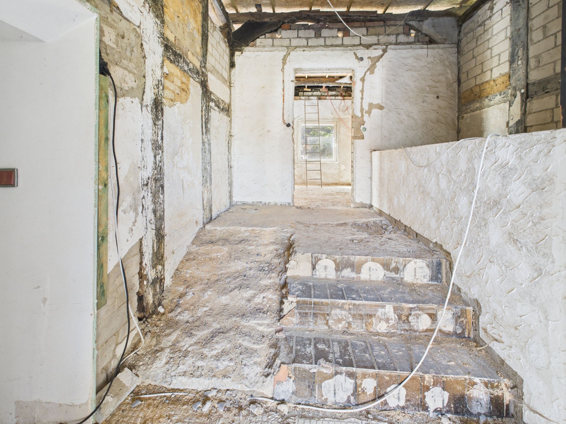 Innenraum eines Hauses im Rohbau mit Treppe und unverputzten Wänden.