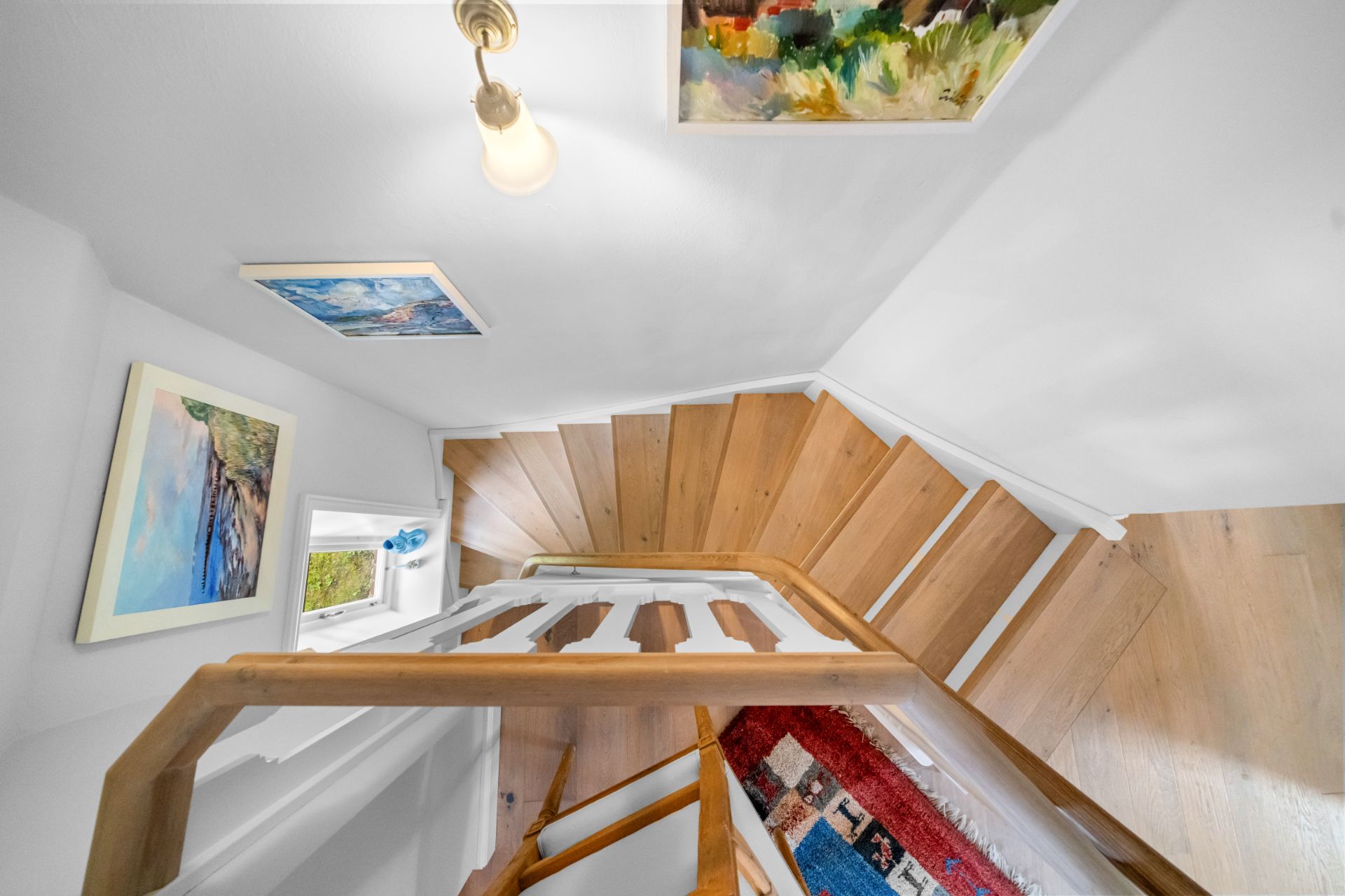 Holztreppe mit weißem Geländer, Gemälden an der Wand und rotem Teppichläufer.
