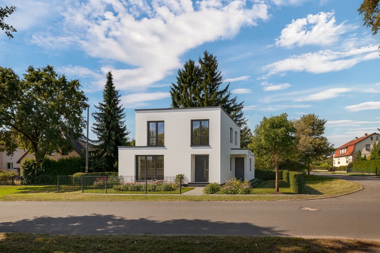 Modernes, weißes Wohnhaus mit flachem Dach und großem Garten an einer ruhigen Straße.