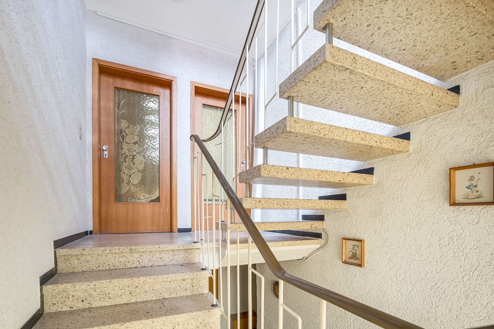 Helle Treppe mit Metallgeländer, zwei Holztüren und dekorativen Bildern an der Wand.