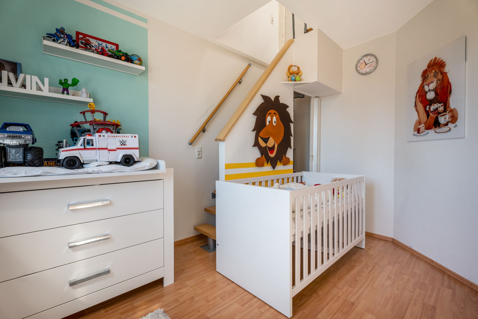Kinderzimmer mit Wickelkommode, Babybett und Wandbild von Löwen.