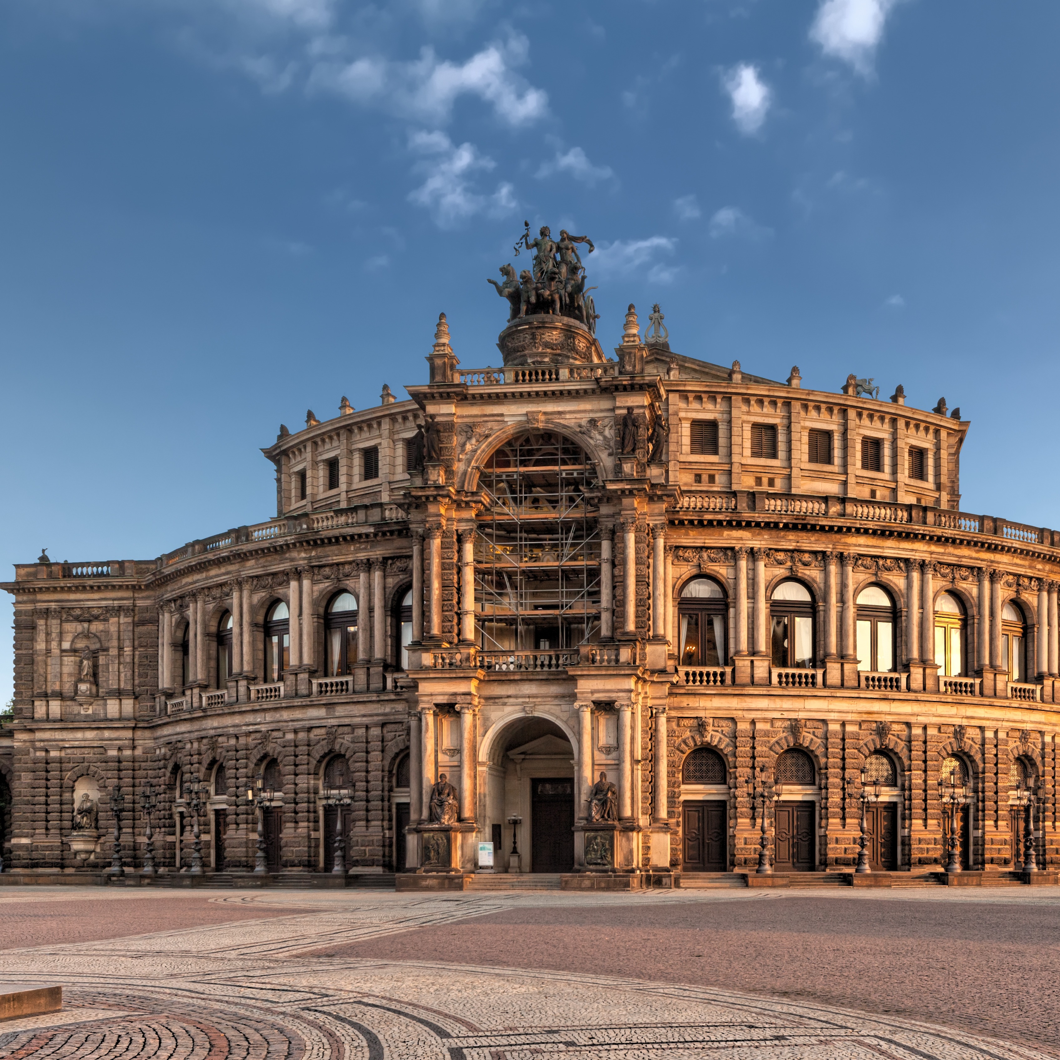 Großes, historisches Gebäude mit Rundbogenfenstern und Figuren auf dem Dach bei Sonnenuntergang.