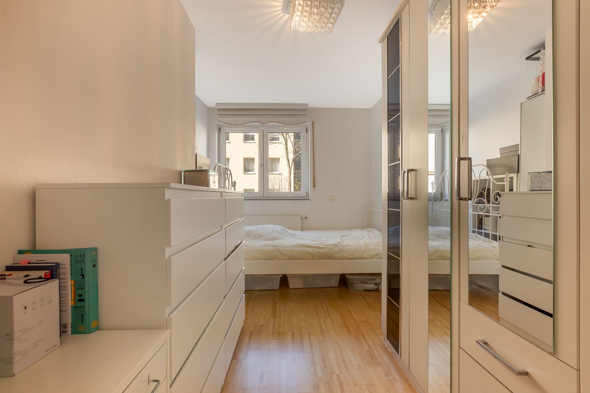 Helles Schlafzimmer mit Doppelbett, weißen Kommoden und Spiegelschrank auf Holzfußboden.