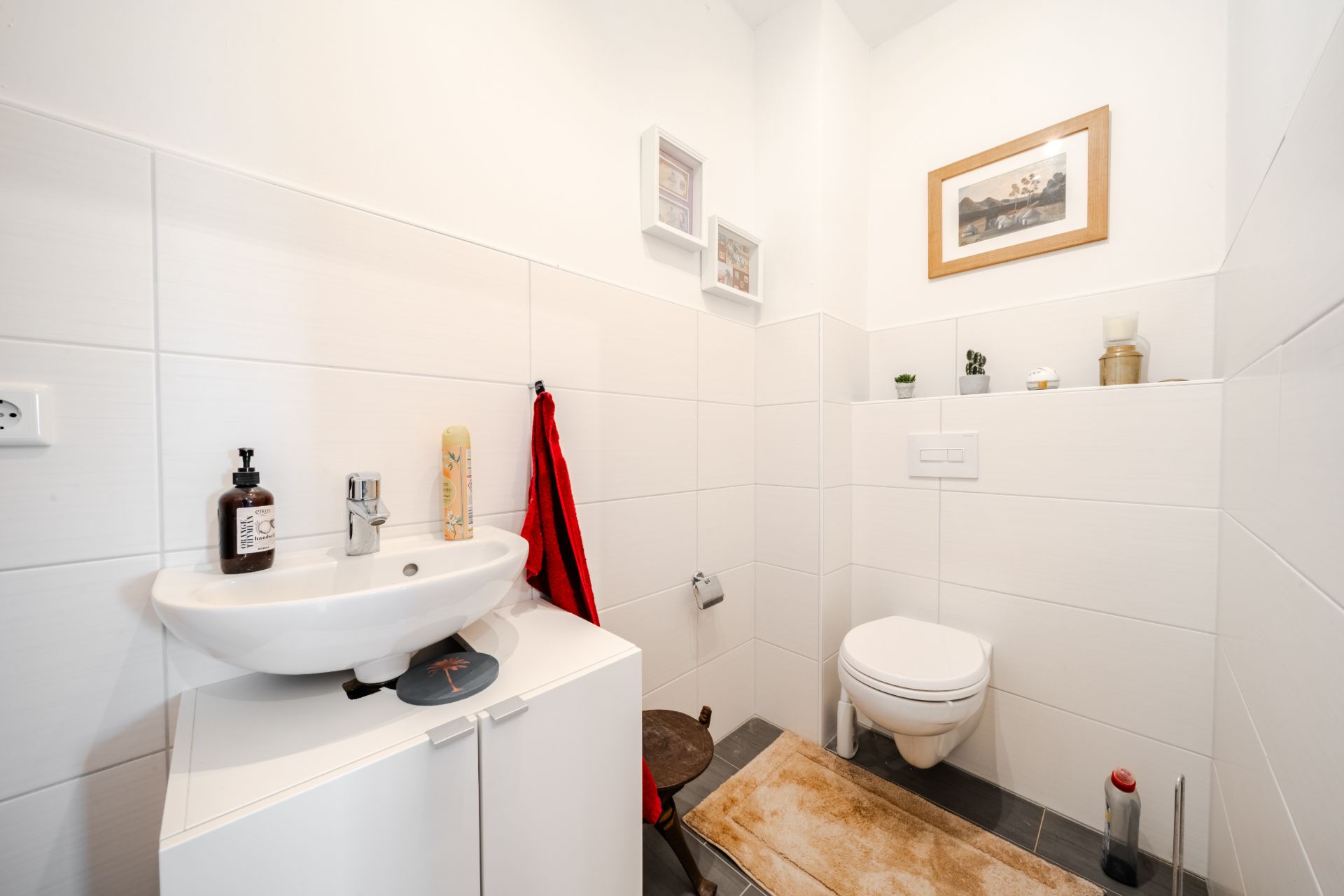 Kleines Badezimmer mit Waschbecken, WC, Spiegel und weißen Fliesen.