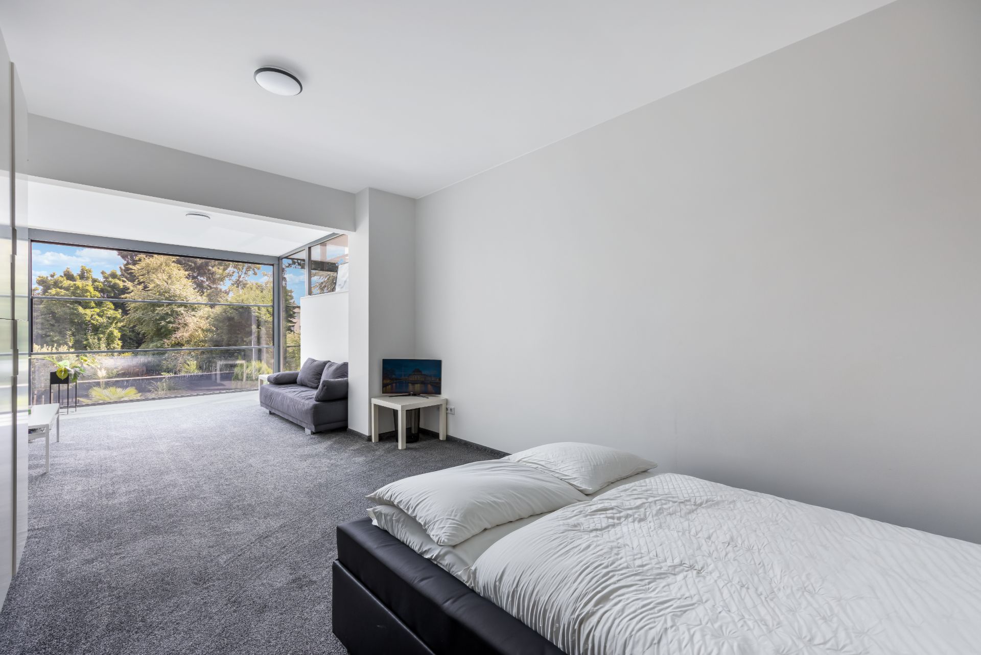 Modernes Schlafzimmer mit großem Fenster, Bett, Sofa und Blick ins Grüne.