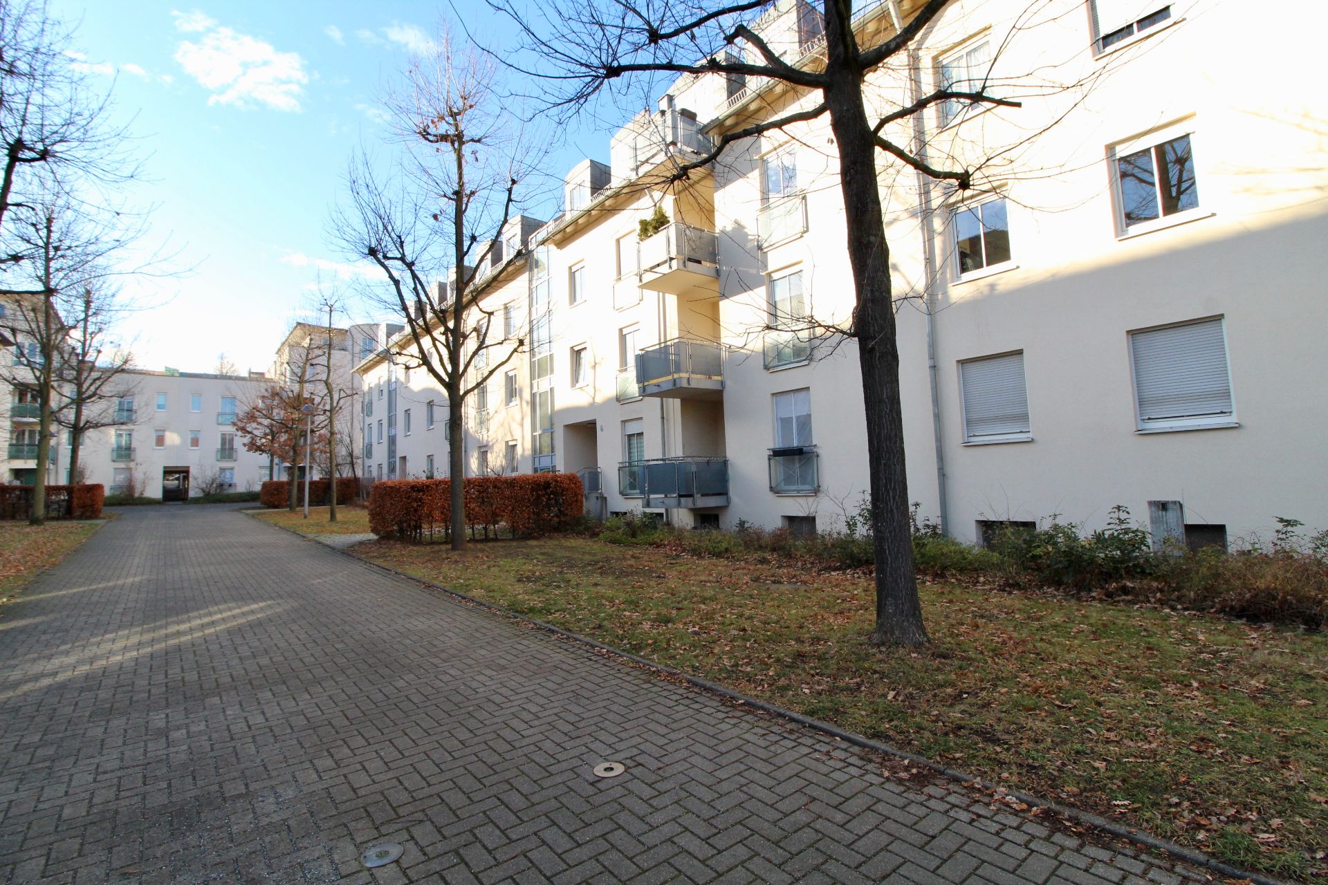 Mehrfamilienhaus mit Balkonen, Gehweg und kahlen Bäumen im Vorgarten.