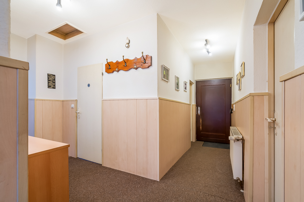 Heller Flur mit Holzvertäfelung, Garderobe, Bildern an den Wänden und brauner Eingangstür.
