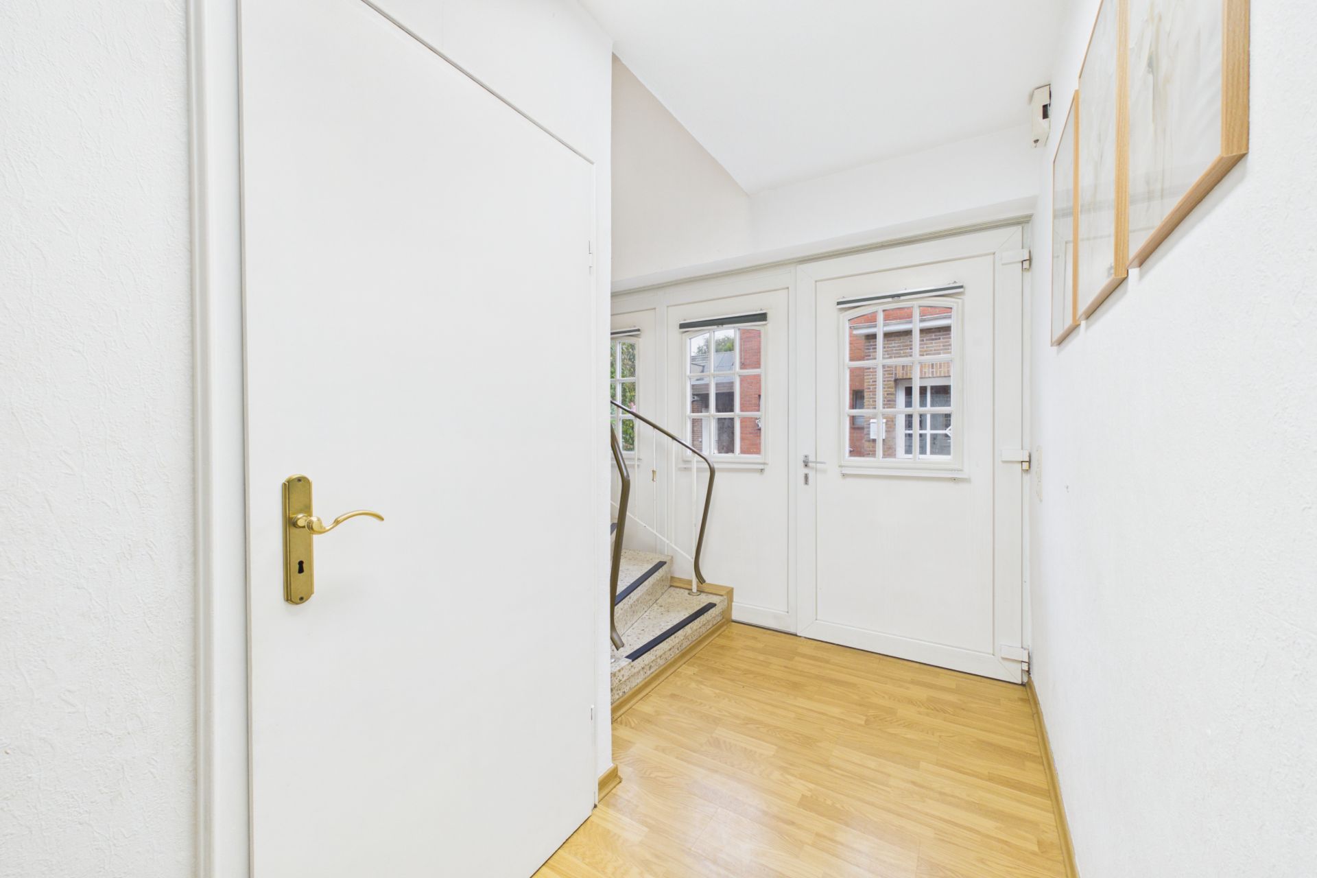 Heller Flur mit Holzboden, weißer Tür und Treppe, Fenster im Hintergrund.
