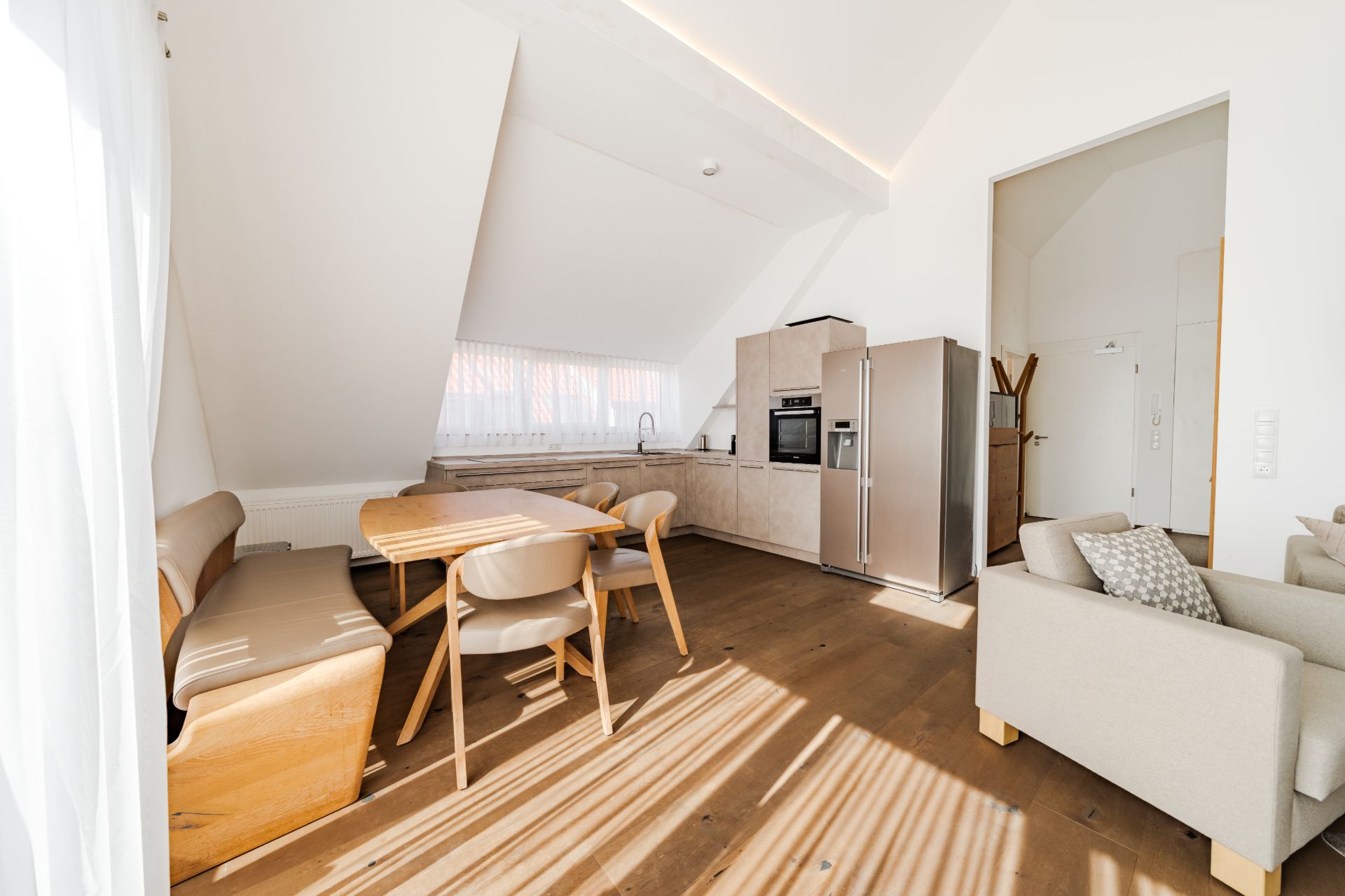 Helle Wohnküche mit Essbereich, Eckbank, Tisch, Stühlen, Sofa und moderner Einbauküche.