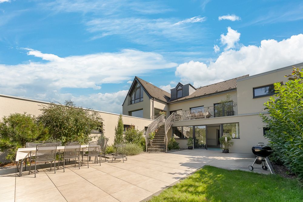 Moderne Terrasse mit Esstisch, Grill und Blick auf ein zweistöckiges Wohnhaus.