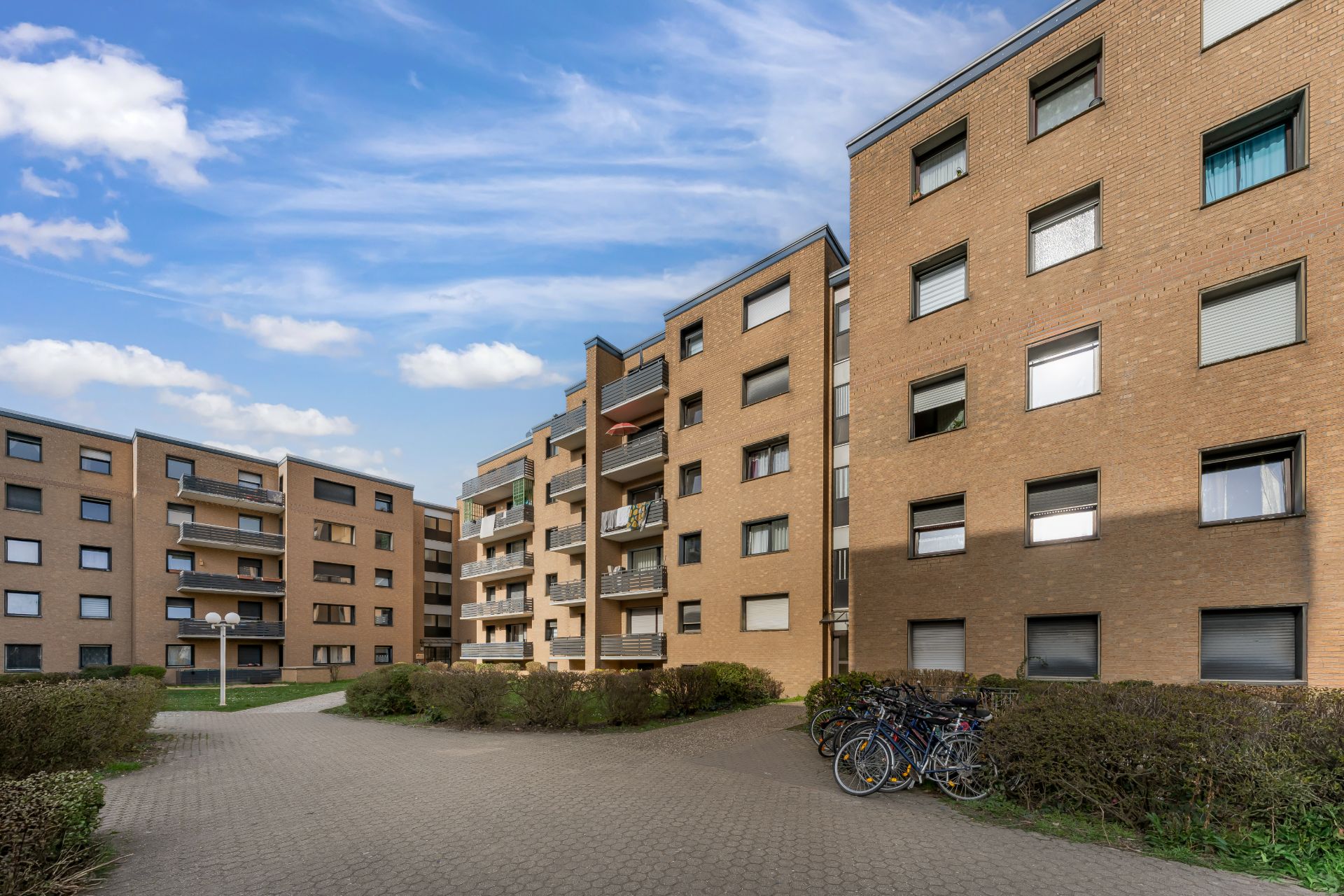 Mehrere Wohngebäude mit Balkonen und Fahrrädern vor dem Eingang, blauer Himmel im Hintergrund.