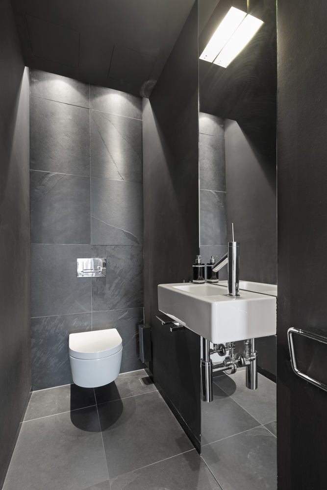 Modernes kleines Bad mit Wandtoilette und rechteckigem Waschbecken, dunkle Fliesen.