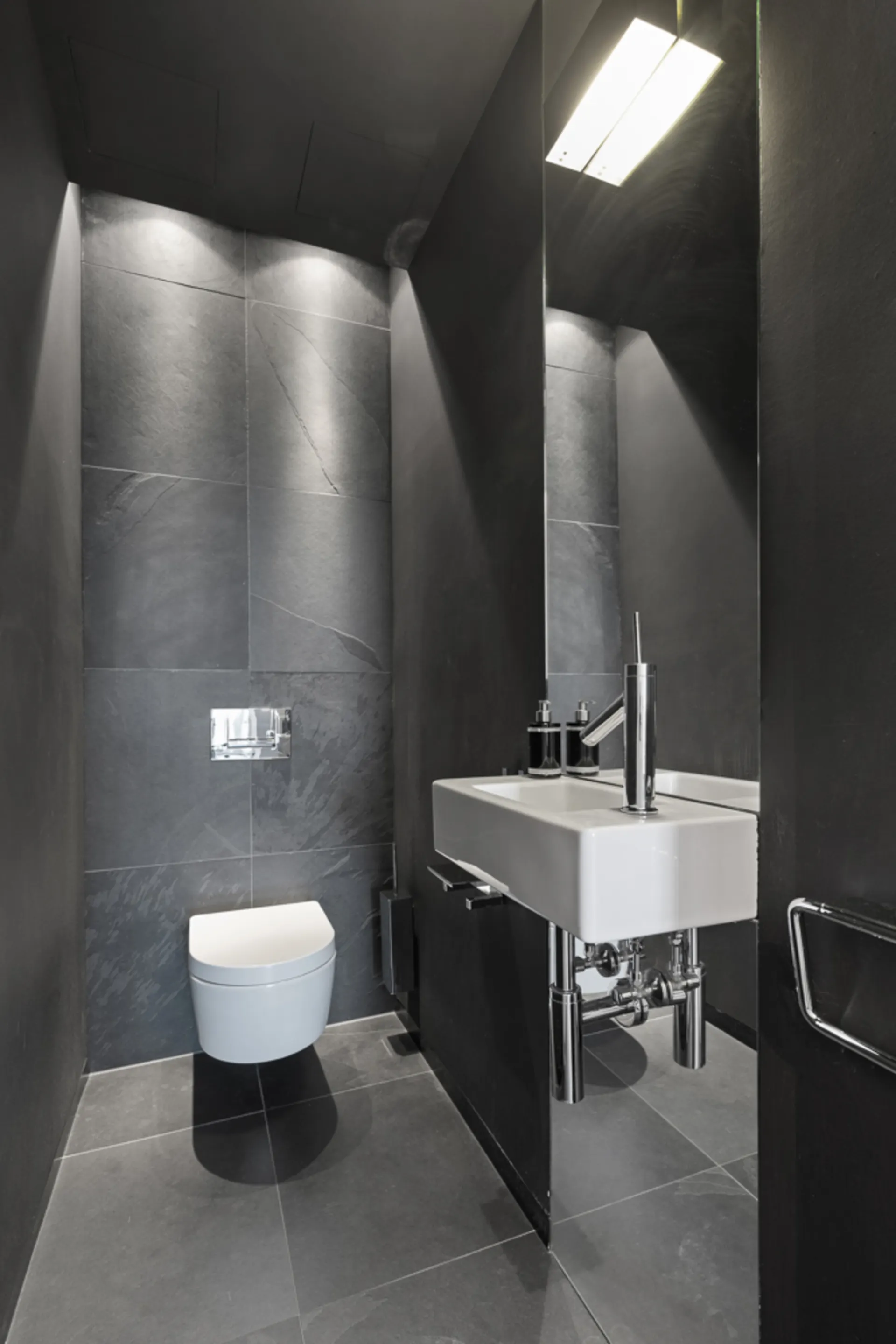 Modernes kleines Bad mit Wandtoilette und rechteckigem Waschbecken, dunkle Fliesen.
