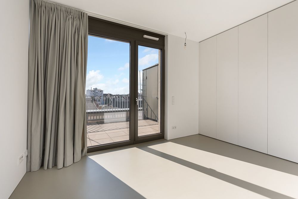 Helles Zimmer mit großem Fenster, Vorhang und Zugang zu einem Balkon mit Stadtblick.