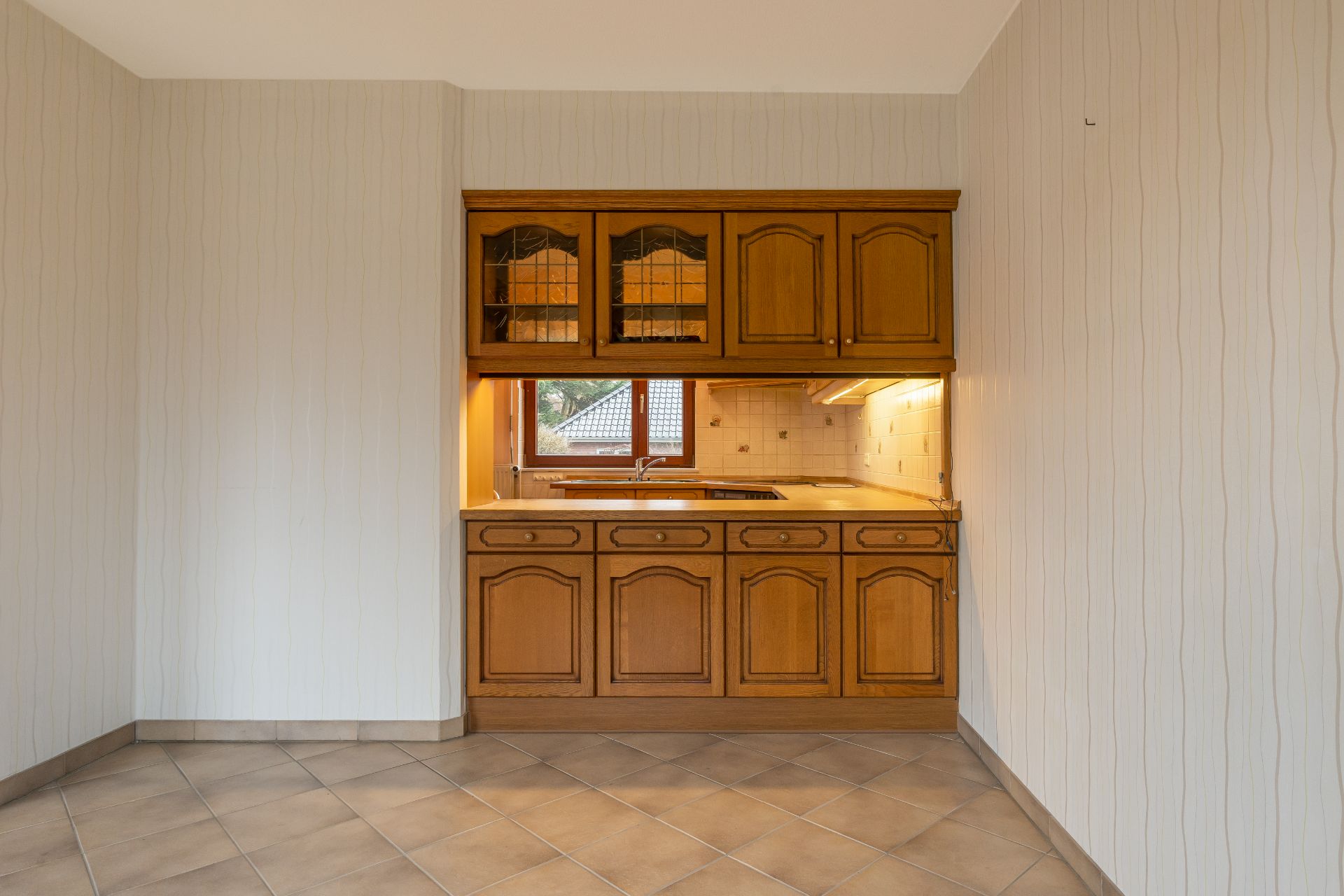 Kleine Küche mit Holzmöbeln, Fliesenspiegel und integriertem Fenster.
