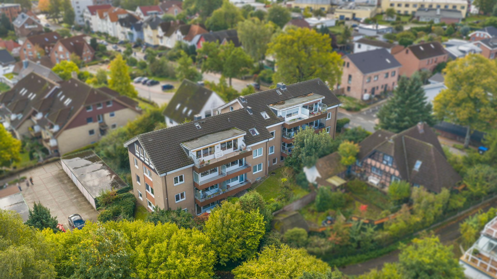 Mehrfamilienhaus mit Balkonen, umgeben von Bäumen und weiteren Wohnhäusern.