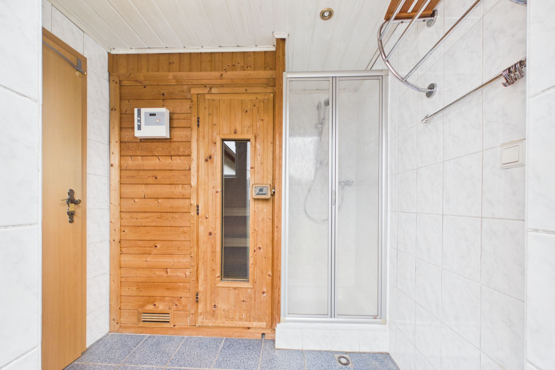 Badezimmer mit Holzsauna und verglaster Duschkabine, weiße Fliesen an den Wänden.